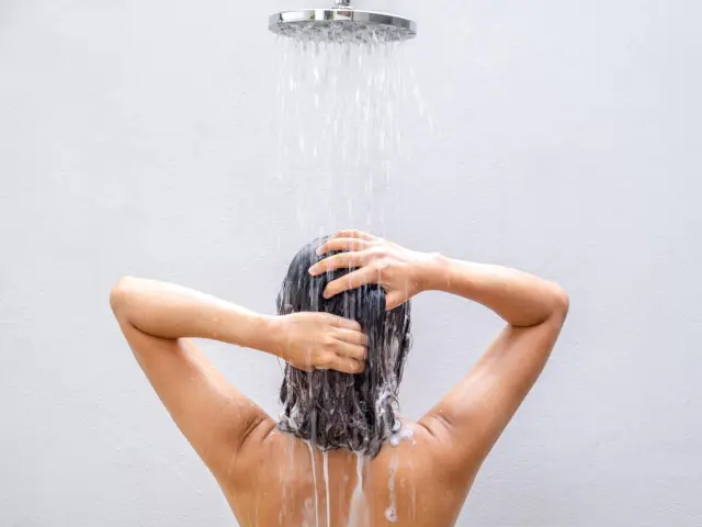 Mujer lavándose el pelo con champú en la ducha.