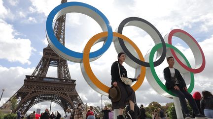 Des touristes devant les anneaux olympiques au pied de la tour Eiffel
