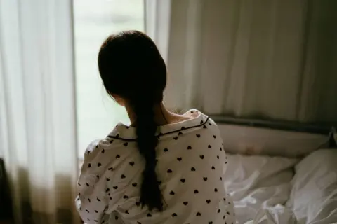 Une adolescente assise sur un lit, regardant par la fenêtre
