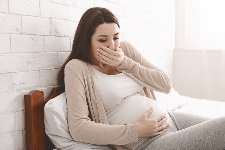 Mal de grossesse. Jeune femme enceinte assise sur le lit, se couvrant la bouche, se sentant nauséeuse pendant la grossesse.