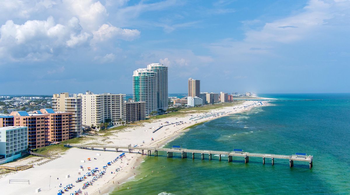 Küste von Orange Beach, Alabama, mit hohen Hotels am Strand und einem Pier, das in das blaue Wasser des Golfs von Mexiko hinausragt.