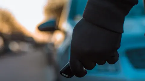 Main gantée de noir tenant une clé à distance devant une voiture floue