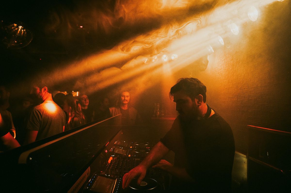DJ dans un club sombre avec des lumières d'ambiance, entouré d'une foule en fête.