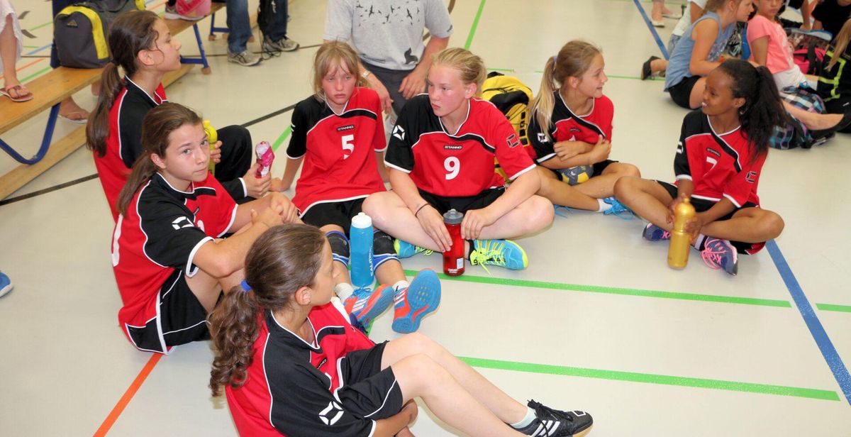 Plusieurs jeunes filles en maillots de sport parlent dans une salle de sport.