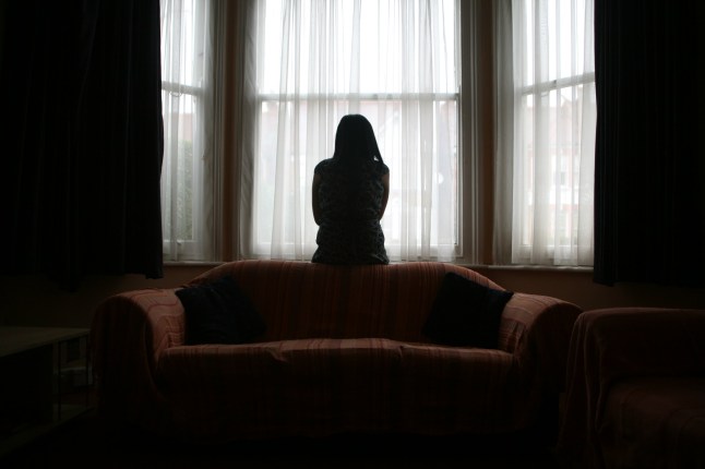 Une jeune femme asiatique souffrant de violence domestique se tient seule dans la fenêtre de sa maison.