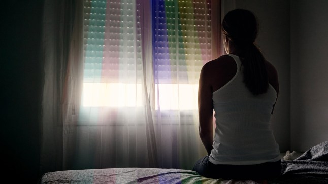 Vue arrière d'une femme abusée assise sur son lit regardant par la fenêtre.