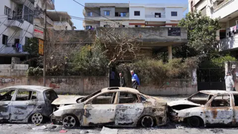 Des gens passent devant des voitures brûlées à Jableh, en Syrie