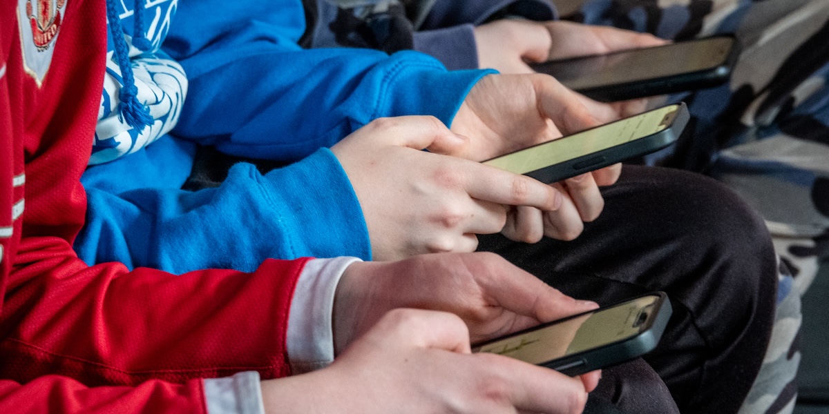 Une photo qui montre les mains de trois garçons assis près d'eux tout en utilisant leurs smartphones