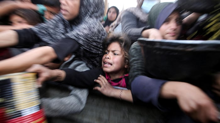 Un jeune fille tend une canne pour recevoir de la nourriture à un comptoir d'aide humanitaire.
