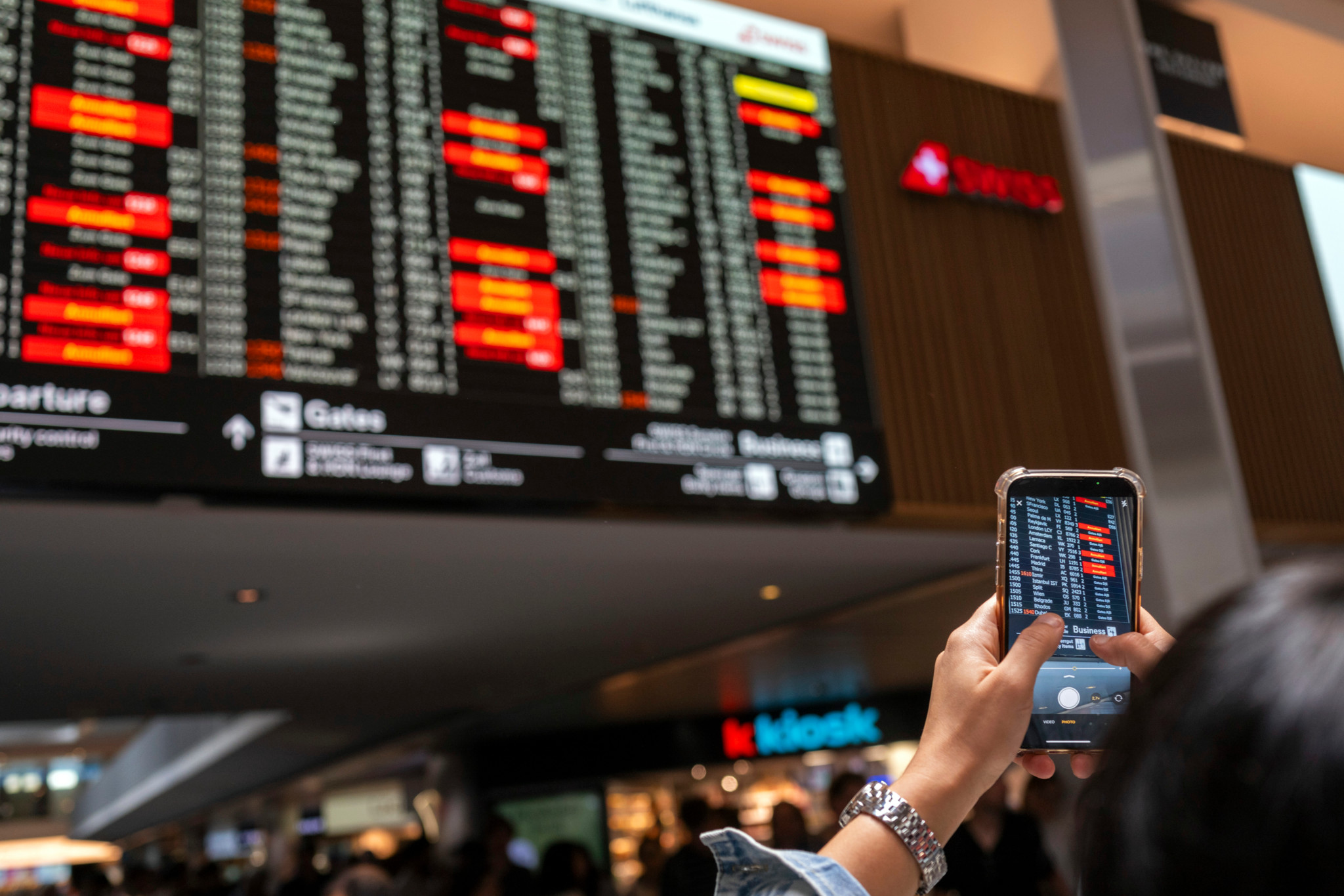 Un passager à l'aéroport de Zurich Kloten photographie avec son téléphone le tableau d'affichage montrant de nombreux vols annulés
