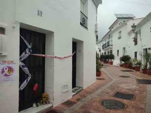 Maison blanche barricadée avec ruban de police, hommages floraux à la porte