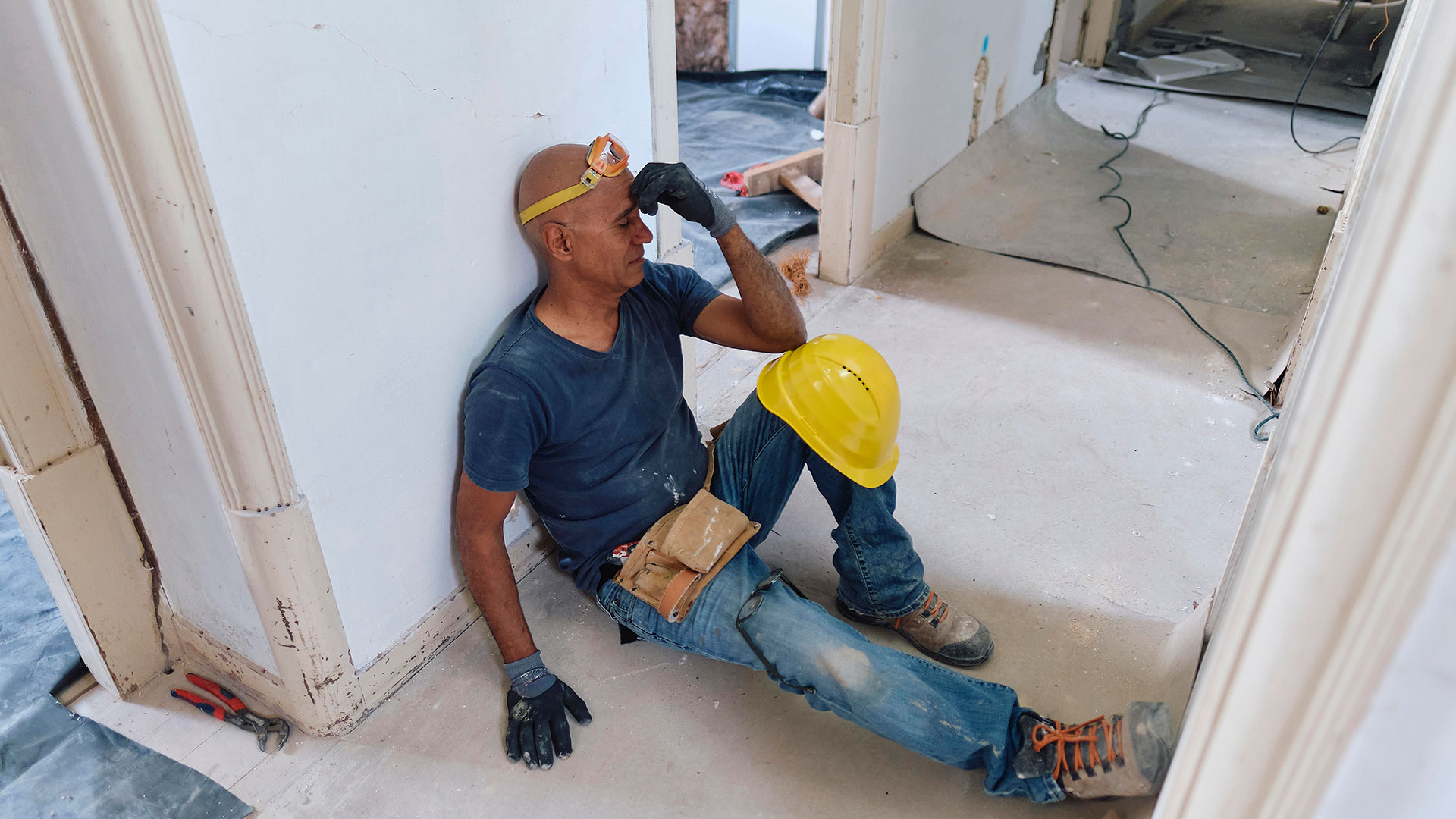 Un ouvrier du bâtiment touche son front et est assis dans un couloir de chantier.
