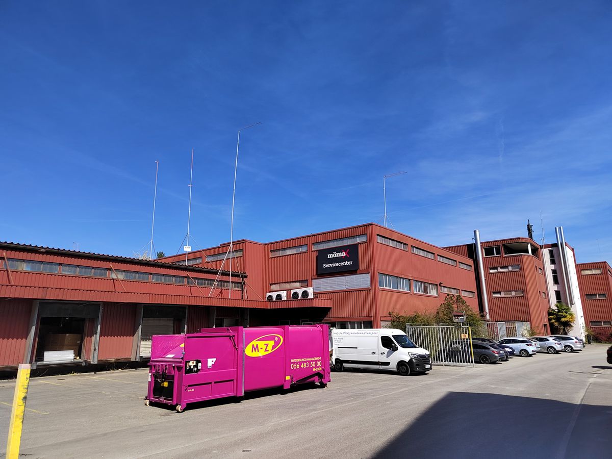 Un container rose sur un site industriel devant un grand bâtiment en briques rouges sous un ciel bleu.
