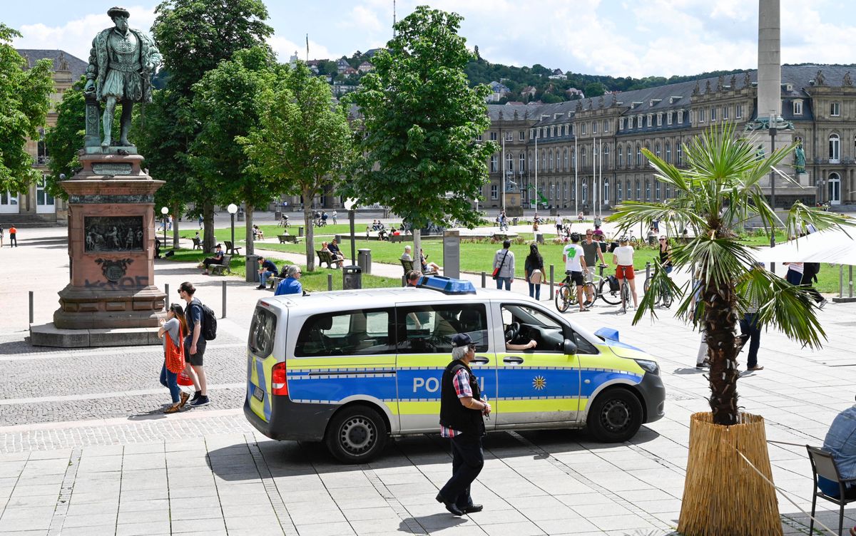 Patrouille de police sur la Schlossplatz à Stuttgart, avec une statue et un bâtiment historique en arrière-plan.