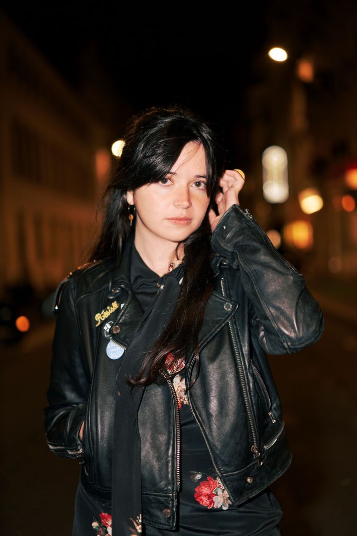 Femme en veste en cuir noir, debout dans une rue éclairée la nuit.