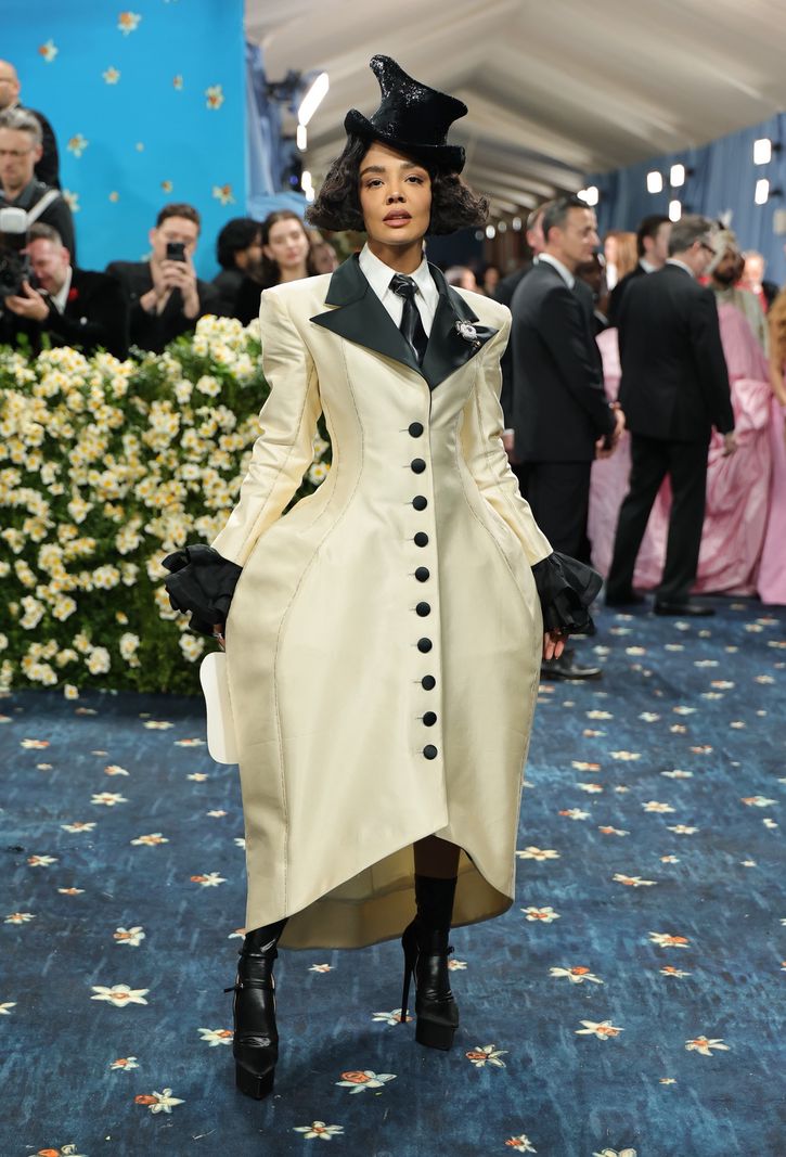 Tessa Thompson au Met Gala 2025, portant une robe longue ivoire avec des boutons noirs et un chapeau noir.
