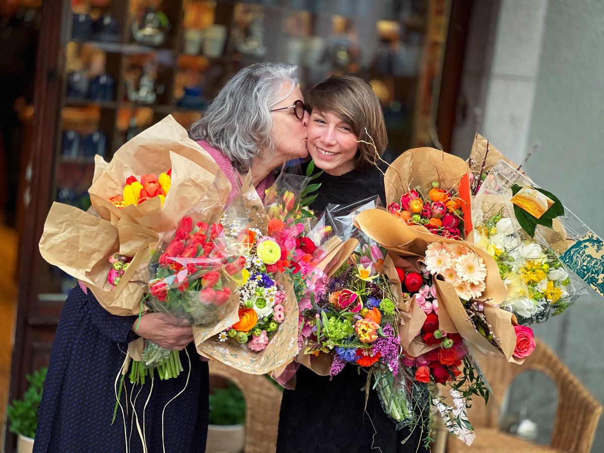 Deux femmes dans une étreinte joyeuse tenant de grands bouquets de fleurs colorées devant le magasin Betjeman & Barton à Carouge.