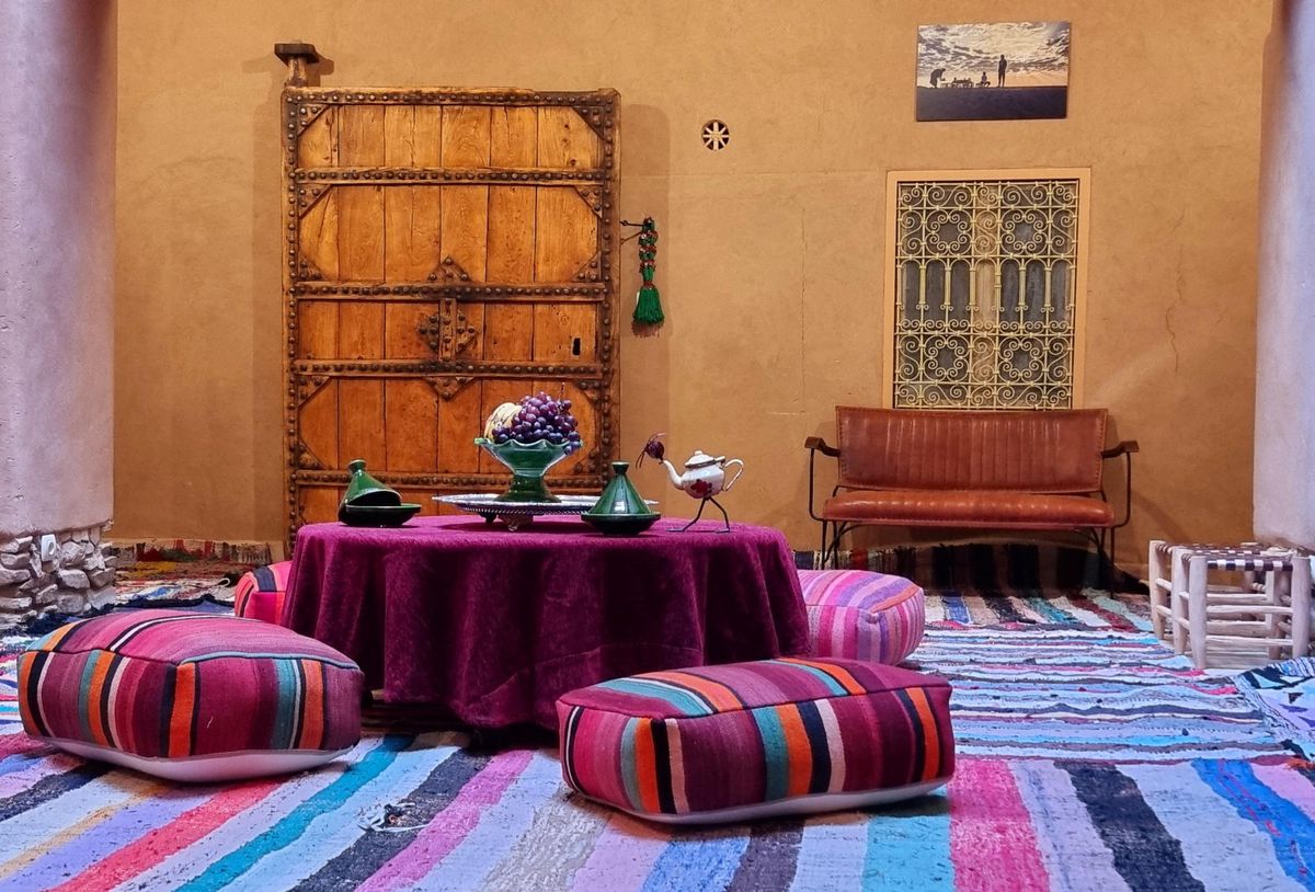 Coin salon marocain traditionnel avec coussins colorés, table basse ronde et décor mural en bois.