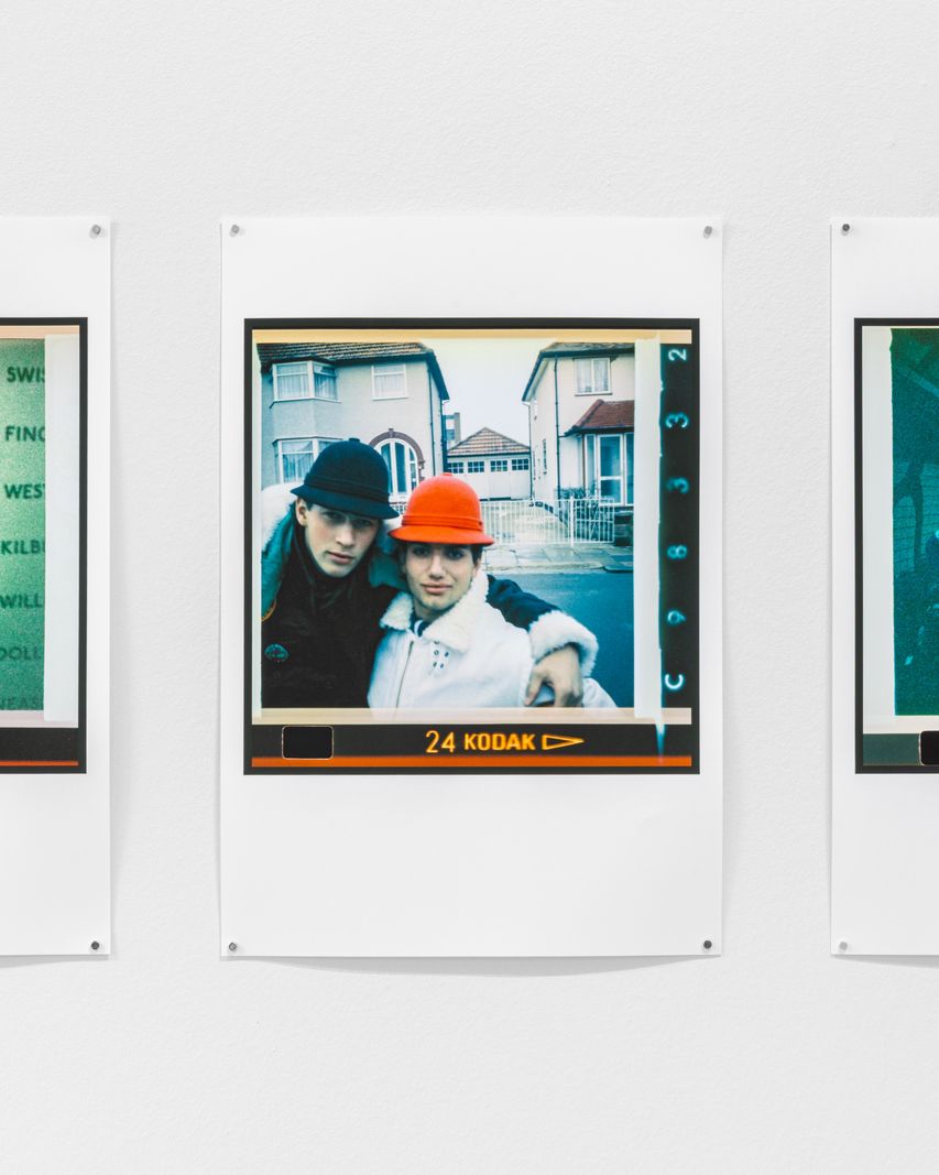 Deux portraits côte à côte sur fond blanc montrant un couple posant devant des maisons, l’un portant un chapeau rouge.