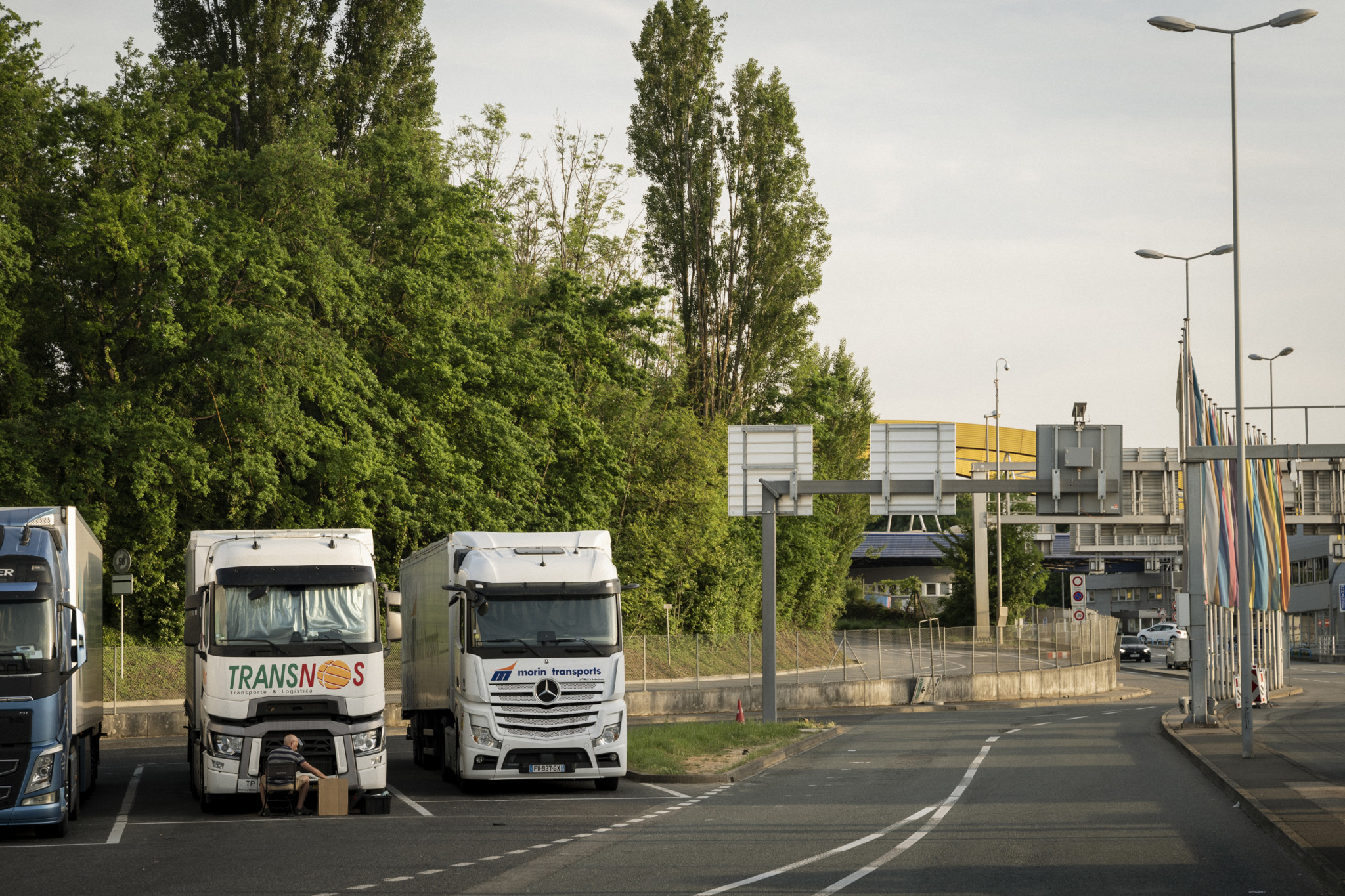 Douane de Bardonnex Camions stationnés près de la douane de Bardonnex à Perly, entourés d’arbres et de panneaux routiers.