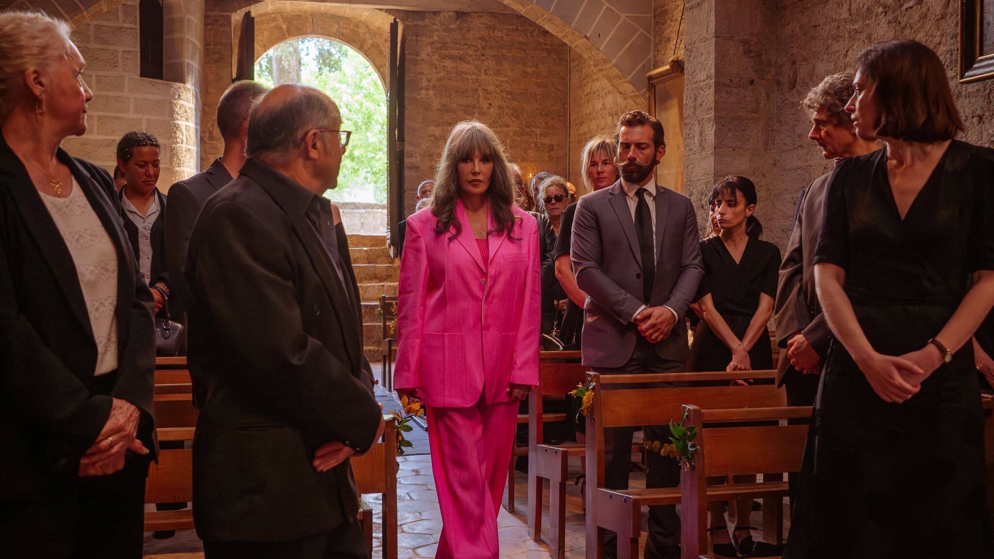 Béatrice Lasserre (Isabelle Adjani) débarque en tailleur rose aux funérailles de son mari Arnaud (Thibault de Montalembert) dans Soleil Noir (Netflix).