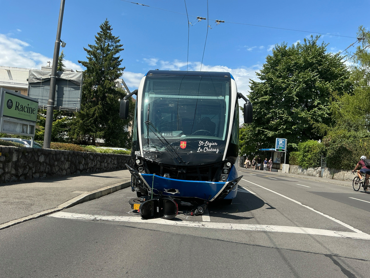 Un tramway St-François – Le Châlet à l’arrêt après une collision, avec des dommages visibles à l’avant, sur une route ensoleillée bordée d’arbres.
