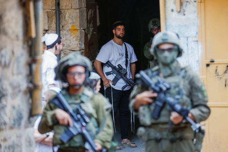 Un colon armé près de troupes israéliennes lors d'une visite hebdomadaire à Hébron