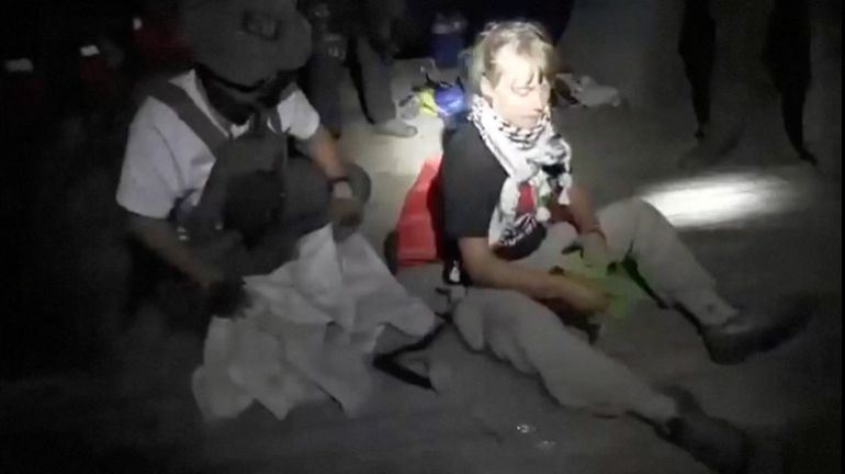 Capture d'écran montrant Greta Thunberg assise à côté d'un membre portant un équipement tactique lors de l'interception des navires de la Flottille, 1 octobre 2025