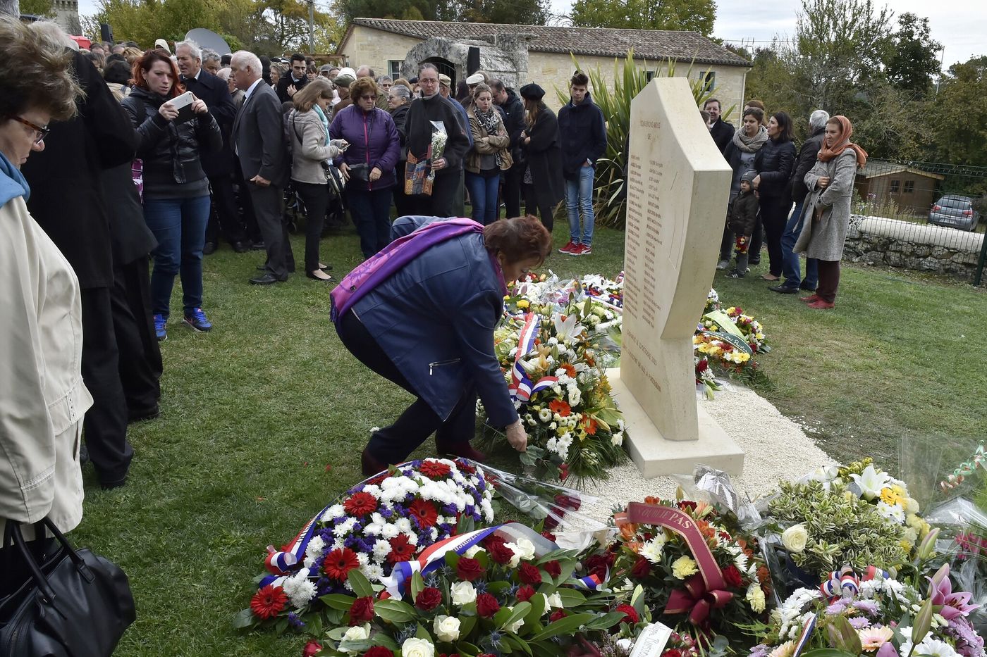 Dépot de fleurs devant une stèle gravée des noms des victimes