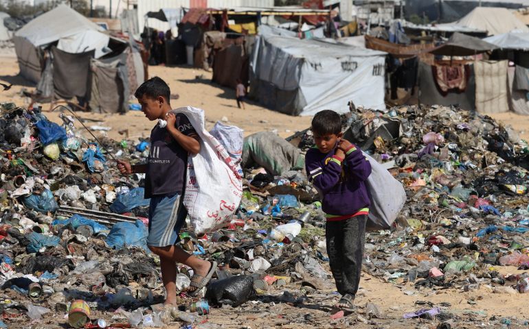 Deux enfants portant des sacs parmi les tas d'ordures entre des tentes à Gaza